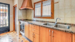 Una cocina con armarios de madera, encimera de granito, pileta de acero inoxidable y una ventana con cortina decorativa.