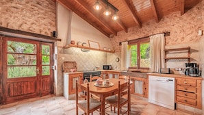 A rustic kitchen with wooden beams, a wooden dining table, and a built-in dishwasher.