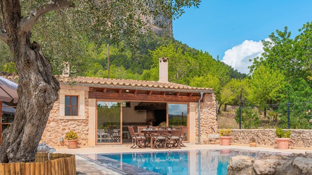 A stone building with a pool, outdoor seating, and a view of a mountain.