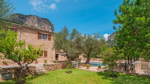 A stone building with a pool, surrounded by trees and a clear sky.