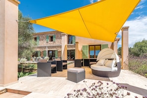 An outdoor patio with wicker furniture, a yellow shade, and a stone building in the background. - Villa 'Los Hibiscus' with Mountain View, Wi-Fi and Air Conditioning (Felanitx)