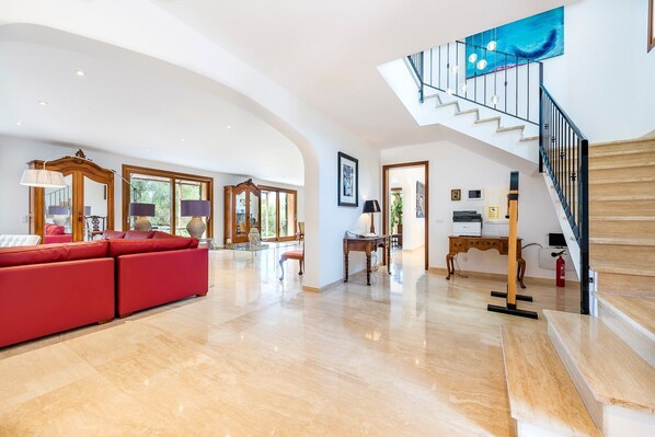 A spacious living area with a red sectional sofa, a staircase with a blue artwork, and a wooden desk.