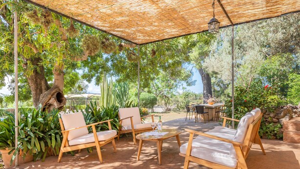 Un patio exterior con mobiliario de madera, una mesa y un farol colgante.