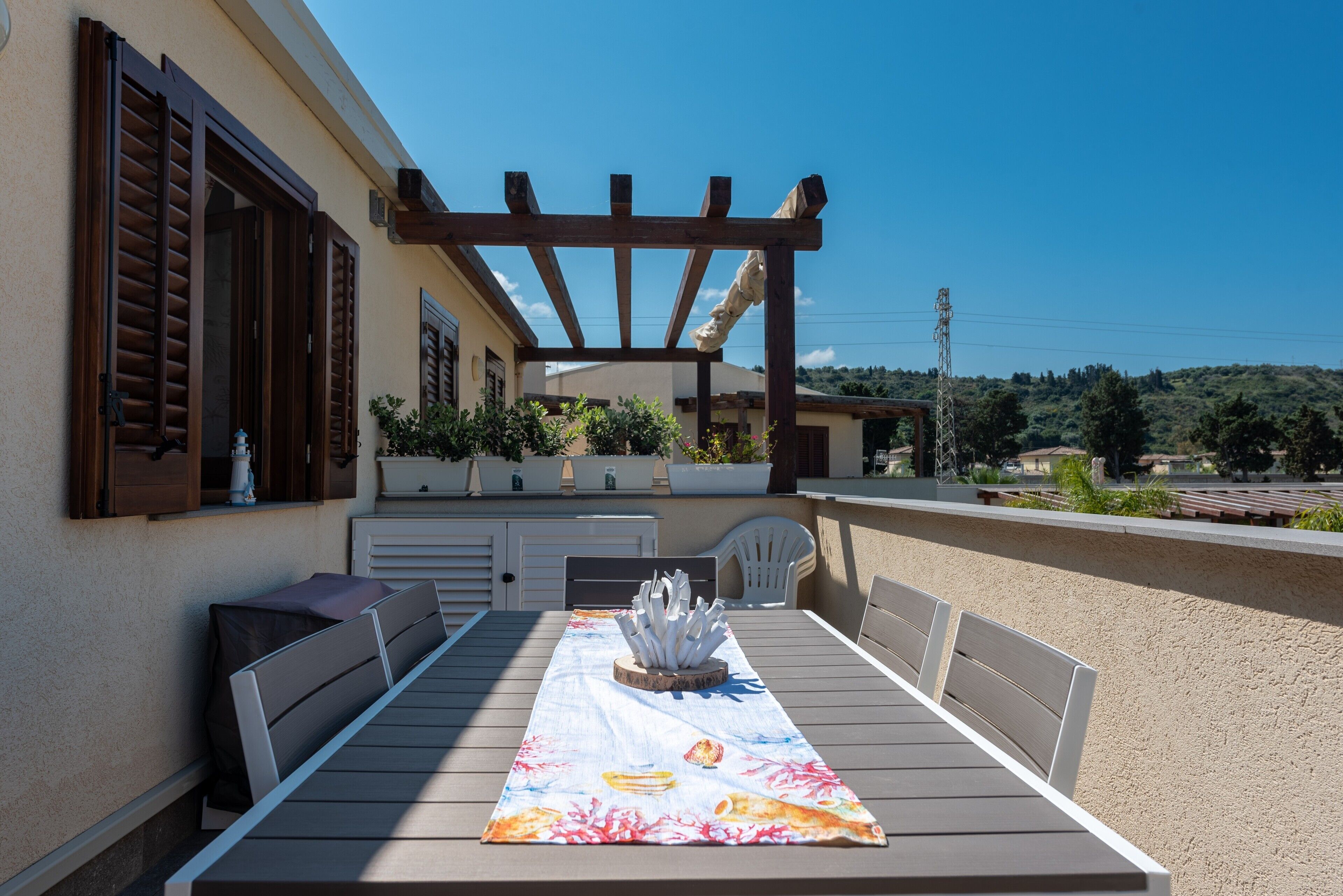 An outdoor patio with a table set for dining, a pergola, and potted plants.
