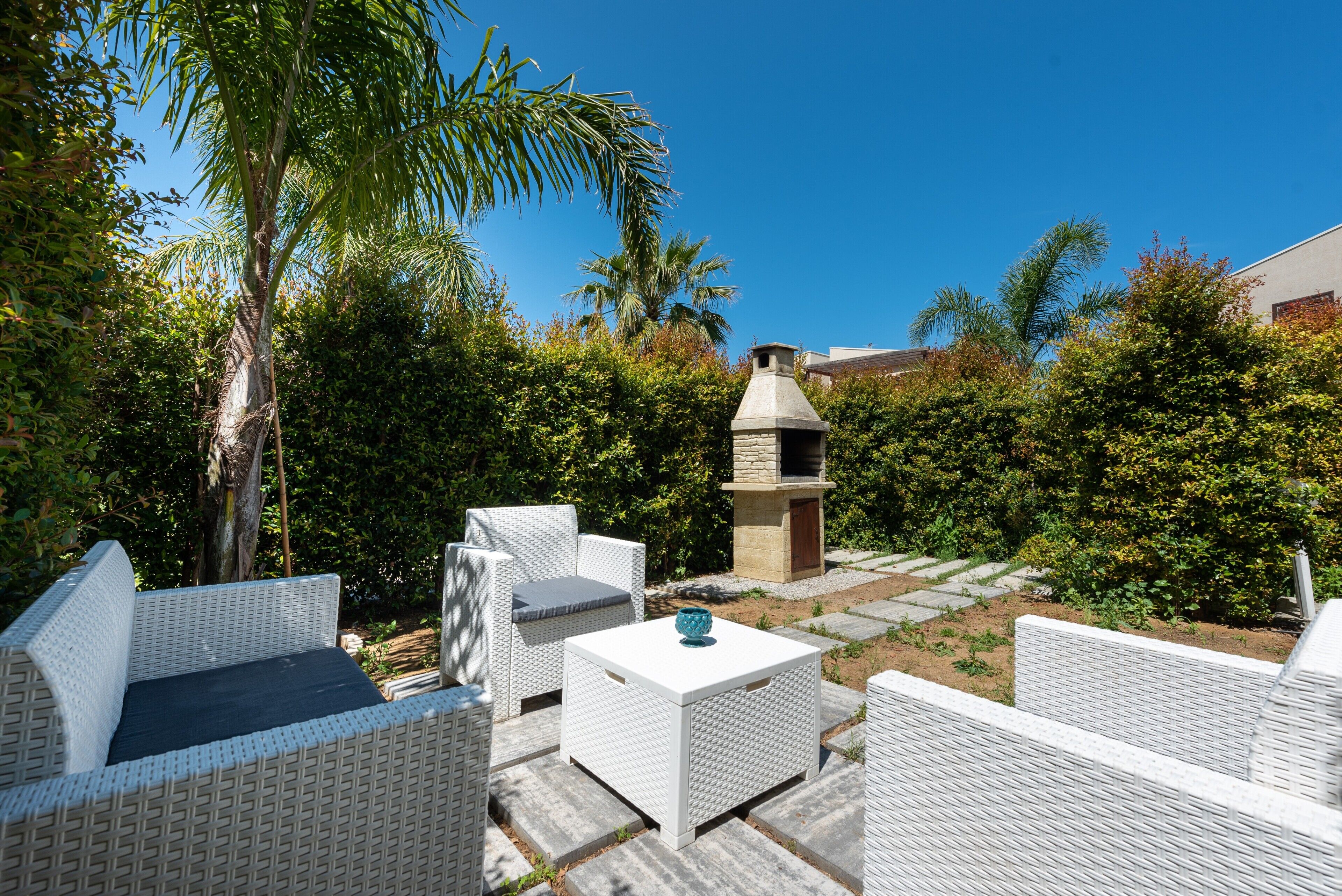 An outdoor patio with wicker furniture, a stone barbecue, and a clear blue sky.