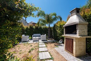 An outdoor patio with a stone barbecue, white wicker furniture, and a stone pathway.