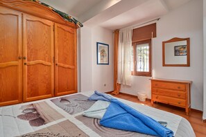Un dormitorio con cama, armario de madera, cómoda y ventana con cortinas.