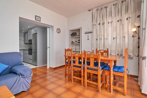 Un comedor con mesa y sillas de madera, un sofá y una cocina al fondo.