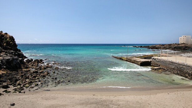 Une plage côtière avec une eau claire, un rivage rocheux et un bâtiment situé sur la droite.