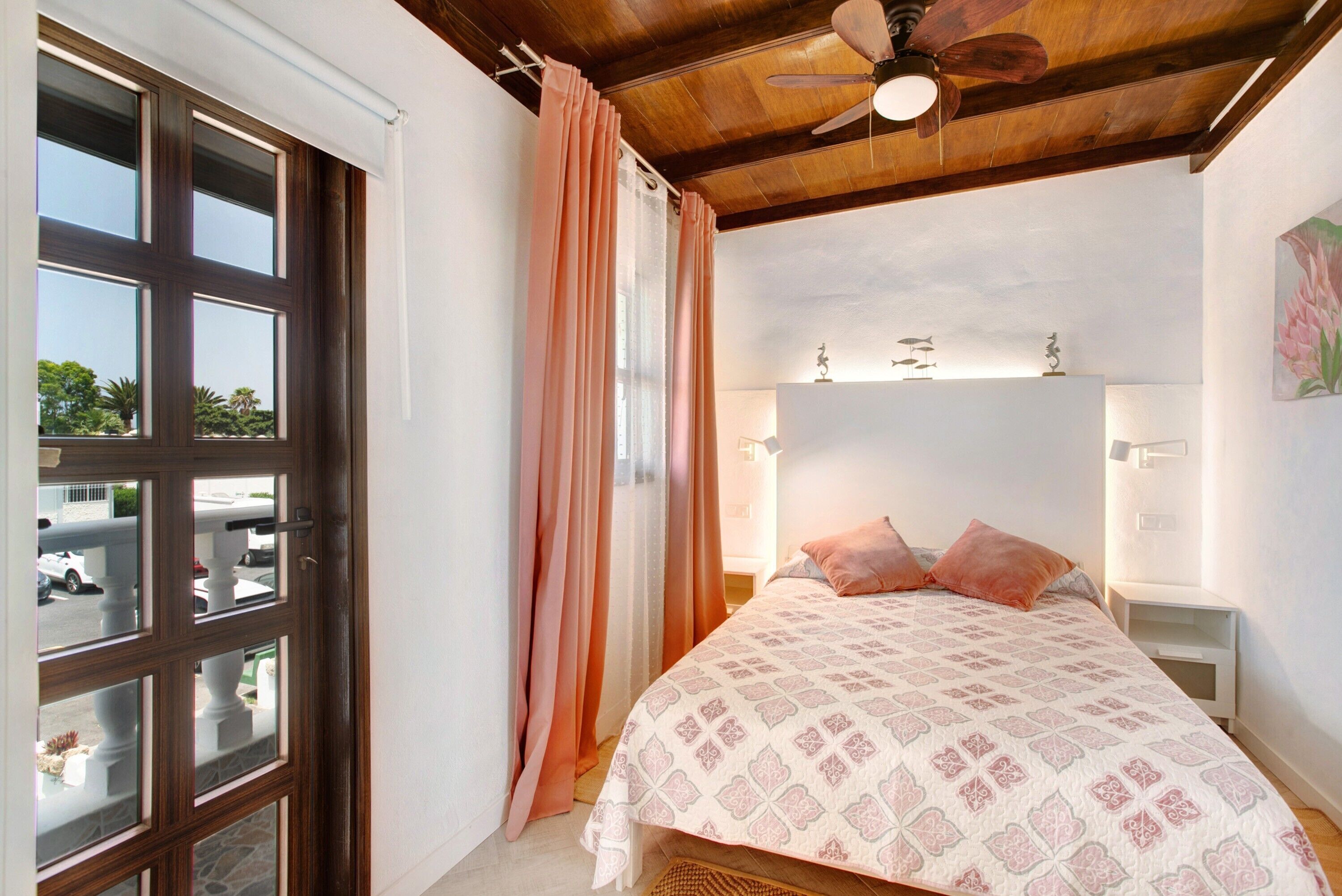 Un dormitorio con una cama, ventilador de techo, mesita de noche y vistas al exterior.
