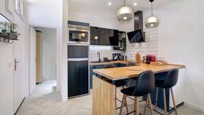 Une cuisine moderne avec un îlot central en bois, des tabourets de bar noirs et des luminaires suspendus.