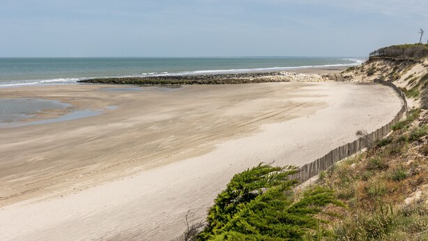 Une plage côtière avec un rivage sablonneux, une digue rocheuse et une clôture en bois.
