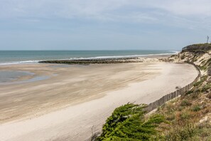 Une plage côtière avec un rivage sablonneux, une digue rocheuse et une clôture en bois.
