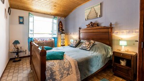 Une chambre avec un plafond en bois, un lit avec une literie à motifs, une table de chevet avec une lampe et une fenêtre donnant sur un beau paysage.