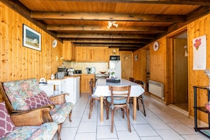 Interior de una cabaña de madera con una mesa de comedor, sillas, un sofá y una zona de cocina.