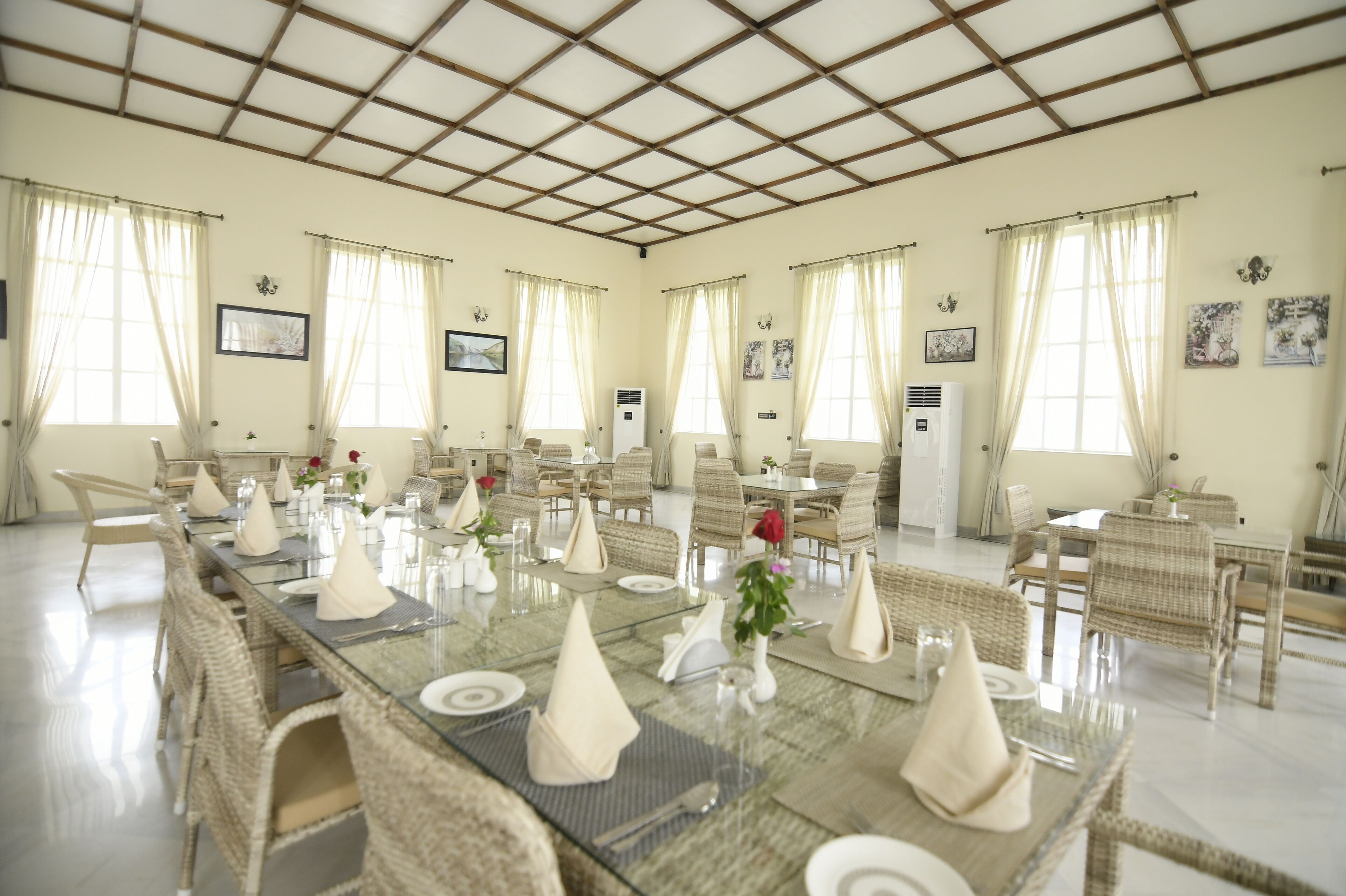 Un comedor con varias mesas dispuestas para comer, con tapas de vidrio y sillas de mimbre.