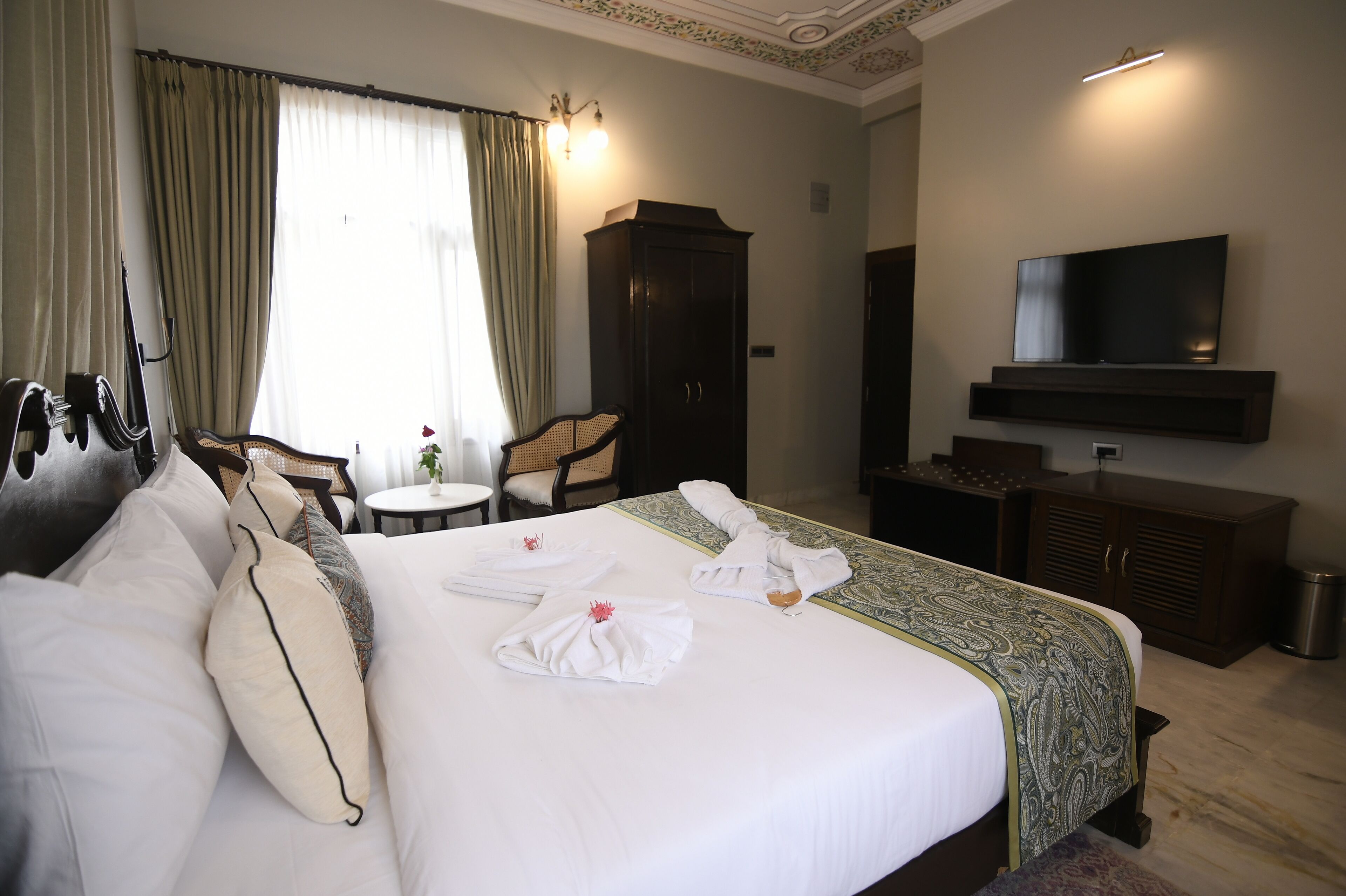 A hotel room with a large bed, a TV mounted on the wall, a wardrobe, a chair, and a small table.