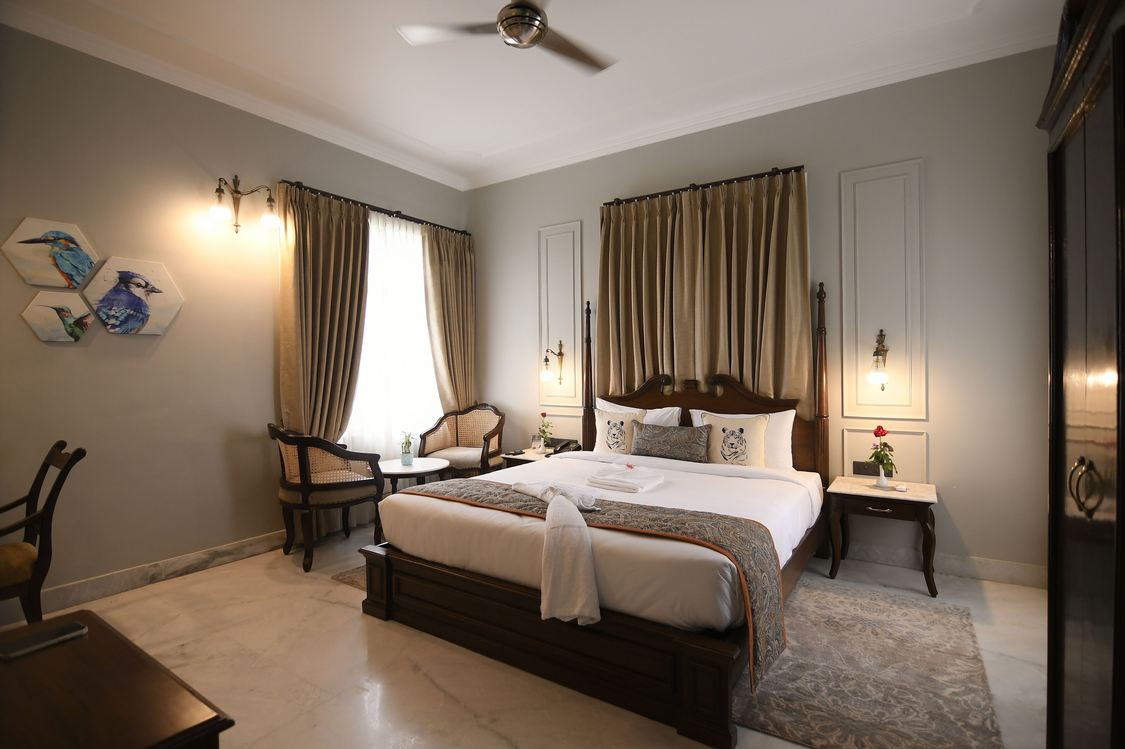 A hotel room with a large bed, a sitting area with a chair and a small table, and a nightstand with a lamp.