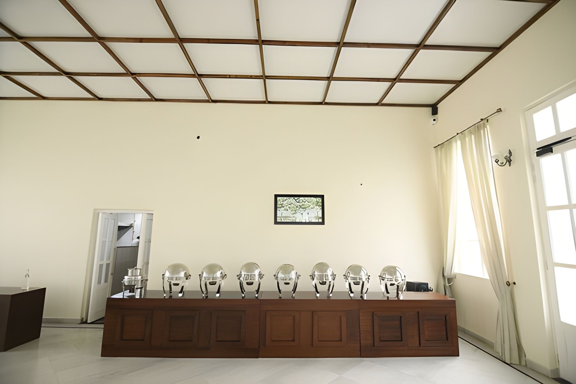A room with a long wooden desk, a framed picture on the wall, and a door with curtains.