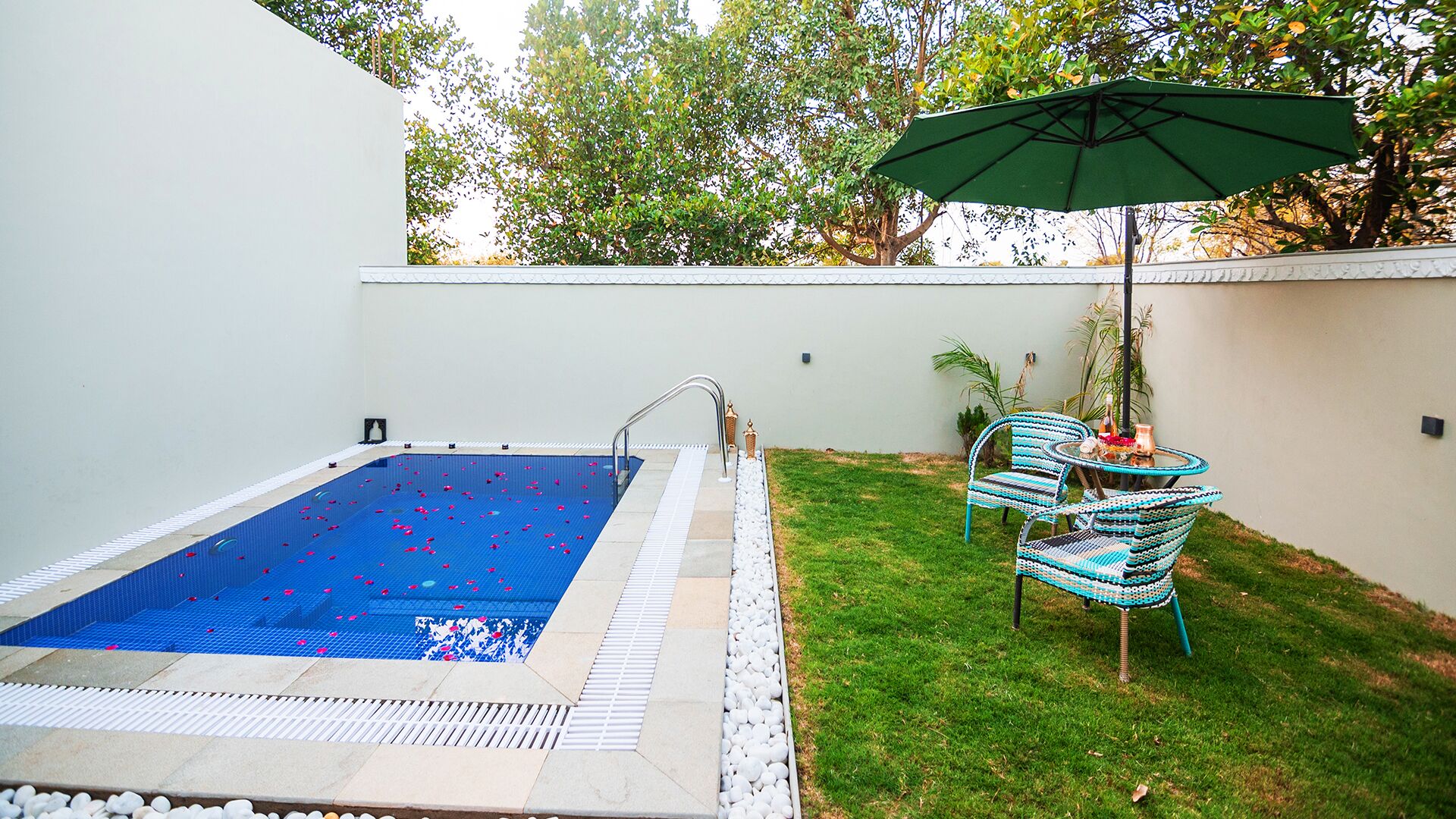 A swimming pool with a tiled deck, a small table with chairs, and a green umbrella.