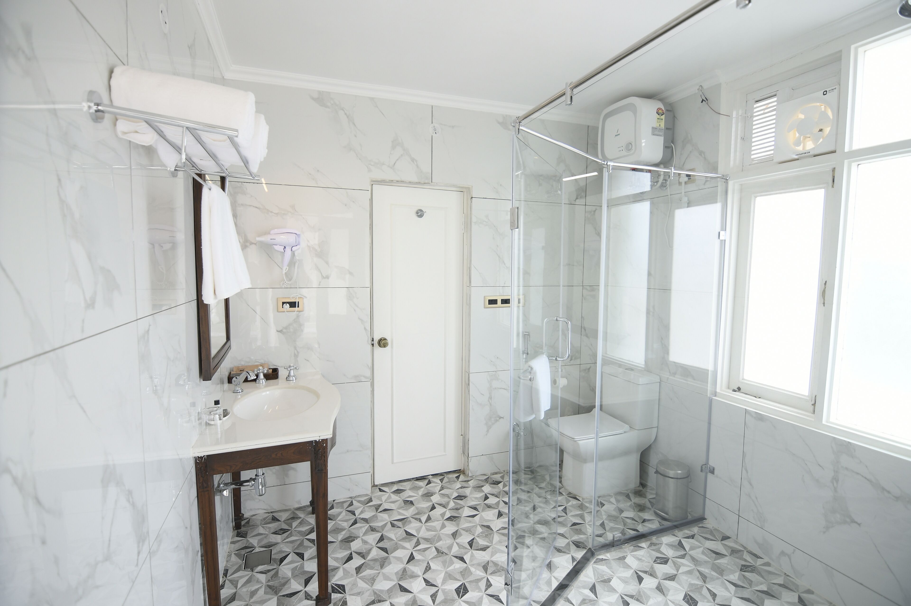 Un baño moderno con ducha de vidrio, un lavabo blanco y piso de mármol.