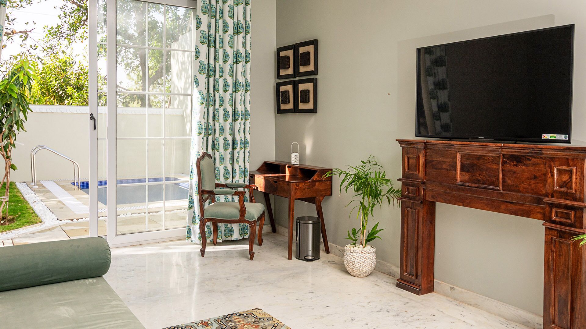 Een woonkamer met een televisie, een houten bureau, een stoel en een potplant.