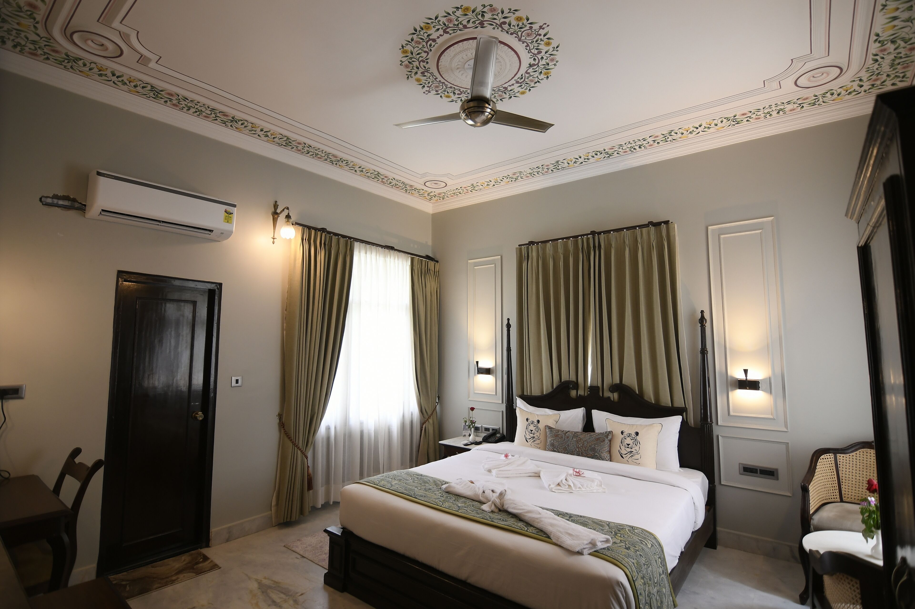 A hotel room with a bed, a desk, a chair, an air conditioning unit, and a ceiling fan.