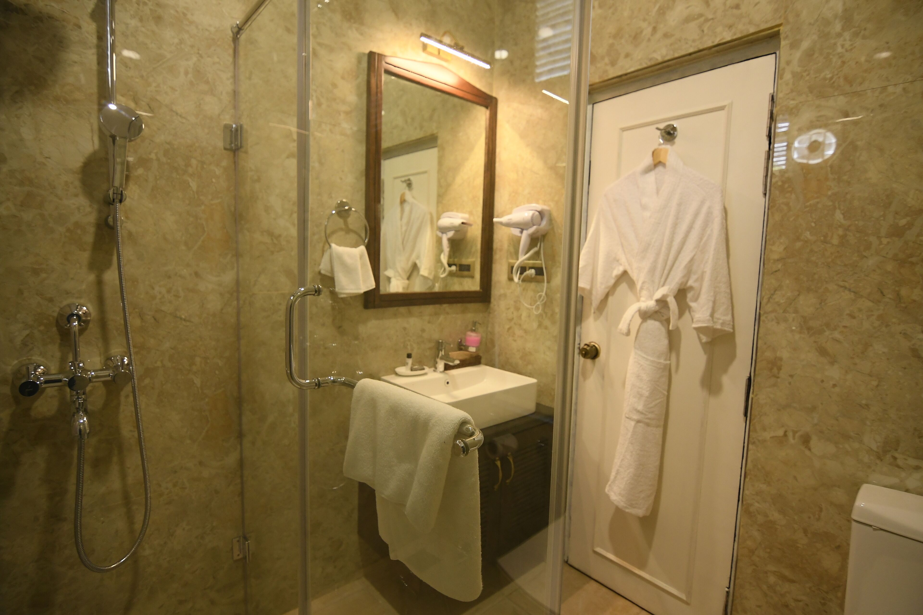 A bathroom with a glass-enclosed shower, a sink with a mirror above it, and a door with a towel hanging on it.