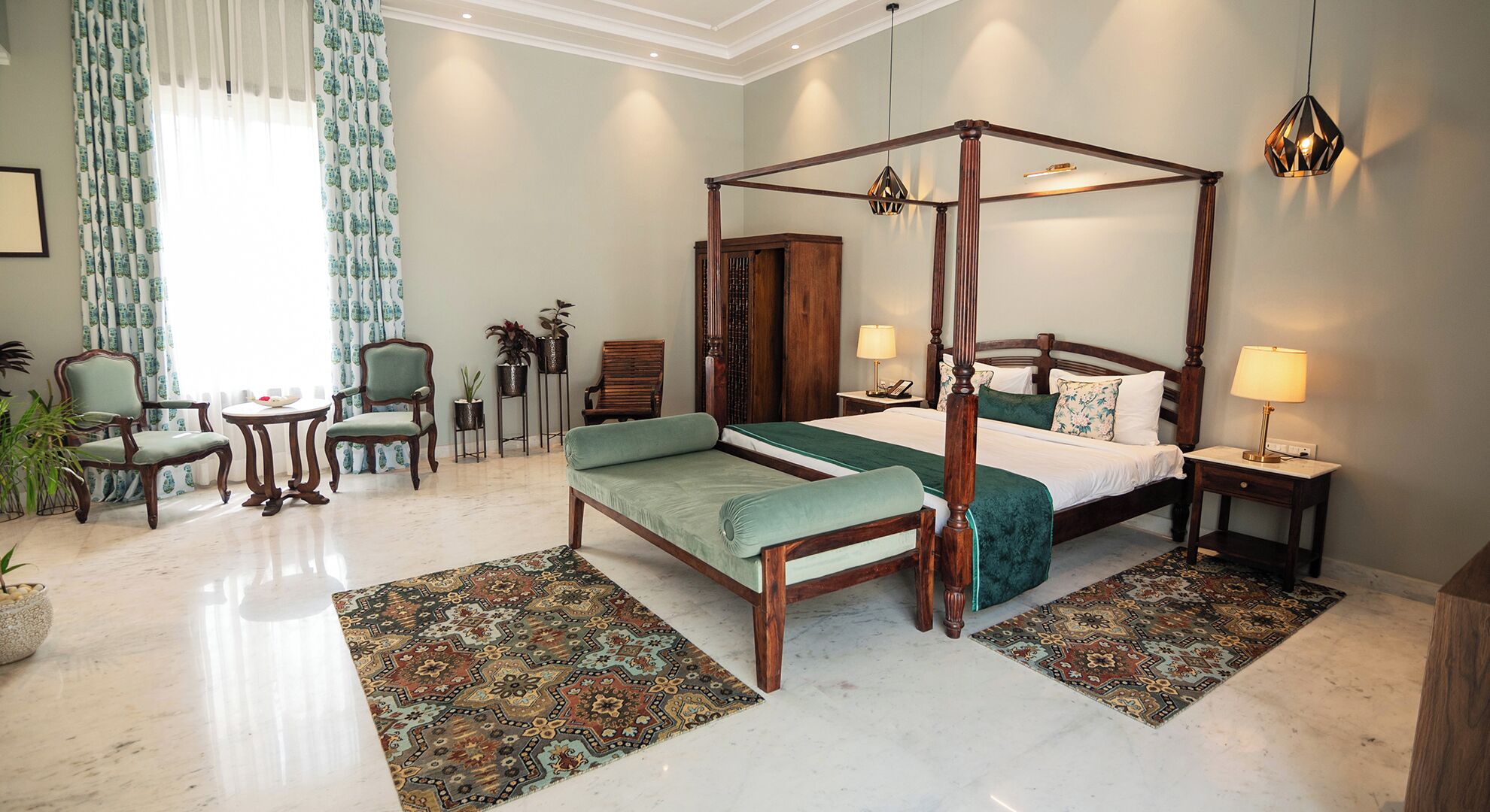 A four-poster bed with a green upholstered bench, a wooden nightstand with a lamp, and a patterned rug on a marble floor.