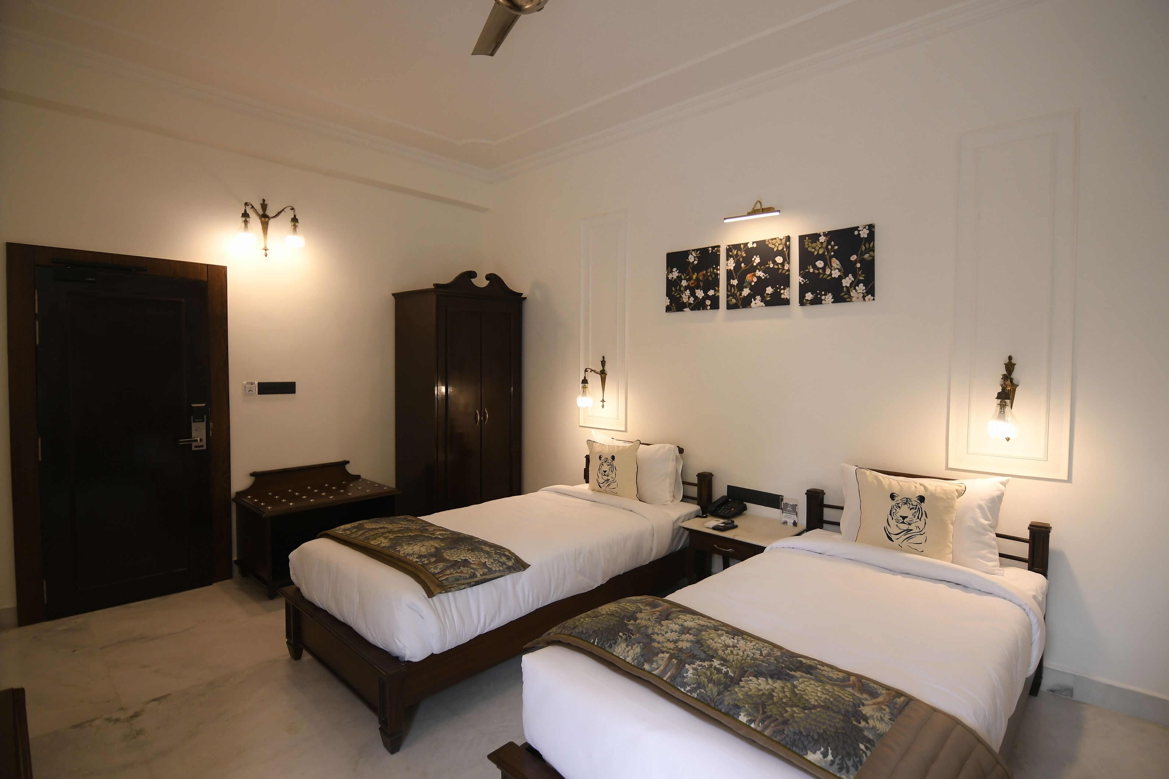 Una habitación de hotel con dos camas, un armario, un escritorio y obras de arte colgadas en la pared.