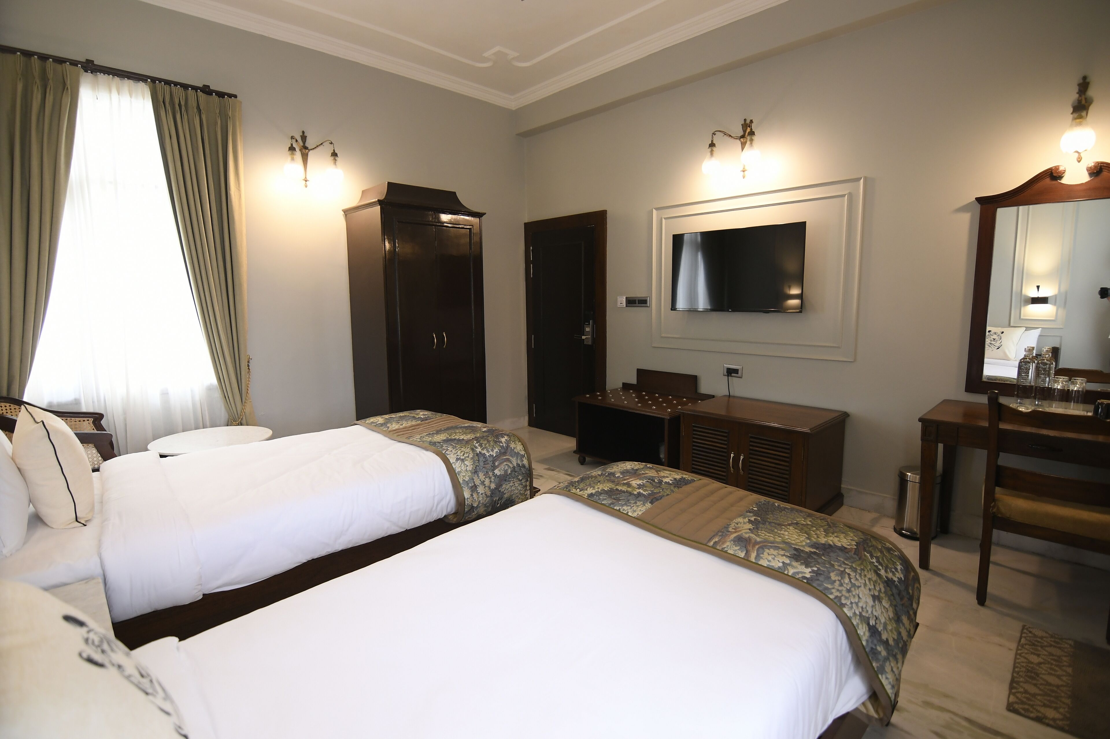 Habitación de hotel con dos camas, televisión, escritorio y espejo.