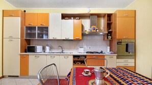 Cocina compacta con microondas, estufa y horno. Hay una mesa de comedor con sillas y un mantel colorido.