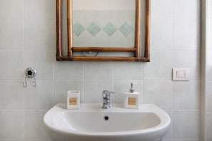 A bathroom with a white sink, two soap dispensers, a mirror with a wooden frame, and a wall-mounted light switch. - Apartment "Colorful" with Mountain View and Private Garden (Colico)