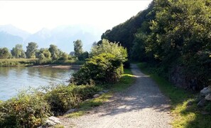 A gravel path beside a river with dense greenery and mountains in the background. - Apartment "Colorful" with Mountain View and Private Garden (Colico)