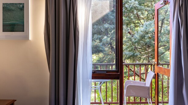 Un dormitorio con un ventanal grande, una cama, una silla y vistas a árboles.