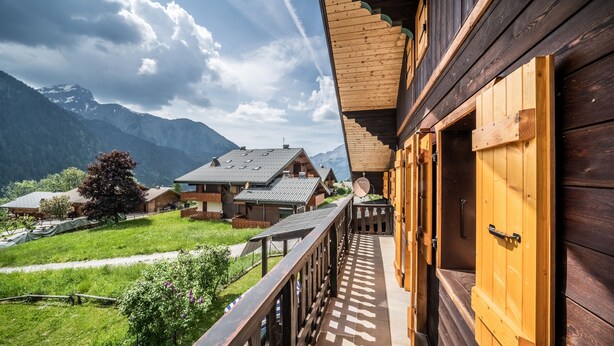 Une cabane en bois dotée d’un balcon donnant sur un paysage montagneux.