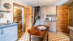 Une cuisine avec un carrelage à motifs, des placards en bois, une table à manger avec un plateau, un four à micro-ondes et un escalier menant à un autre niveau.