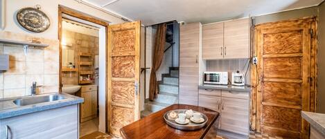 A kitchen with a checkered floor, wooden cabinets, a dining table with a tray, a microwave, and a staircase leading to another level.