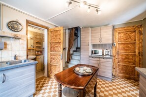 A kitchen with a checkered floor, wooden cabinets, a dining table with a tray, a microwave, and a staircase leading to another level.