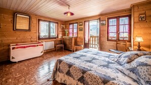Une chambre rustique en bois, avec un lit, une commode, une chaise et une fenêtre donnant sur les montagnes.