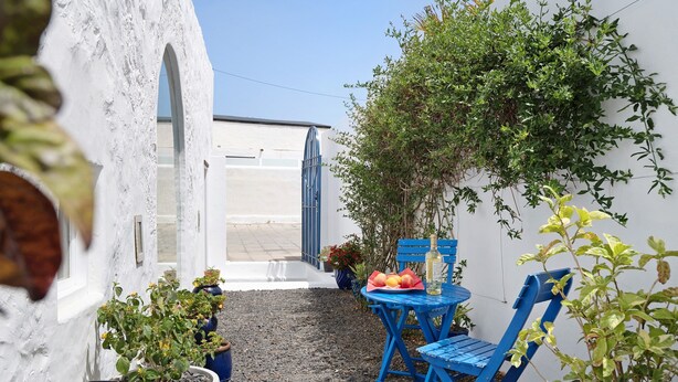 Eine Terrasse mit Tisch, Stühlen, Blumentöpfen und einer weißen Wand mit einem Bogen.