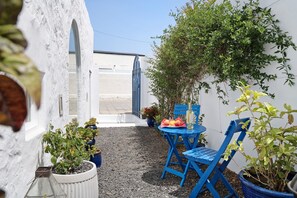 A patio with a table and chairs, potted plants, and a white wall with an archway.