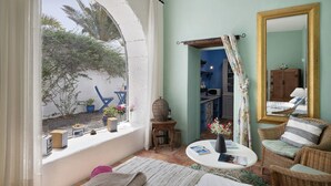 Ein gemütliches Zimmer mit einem großen Bogenfenster, einem Korbstuhl, einem kleinen Tisch und einem Spiegel an der Wand.