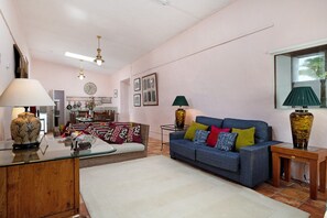A living room with a sofa, a coffee table, a lamp, a vase, and a dining area in the background.