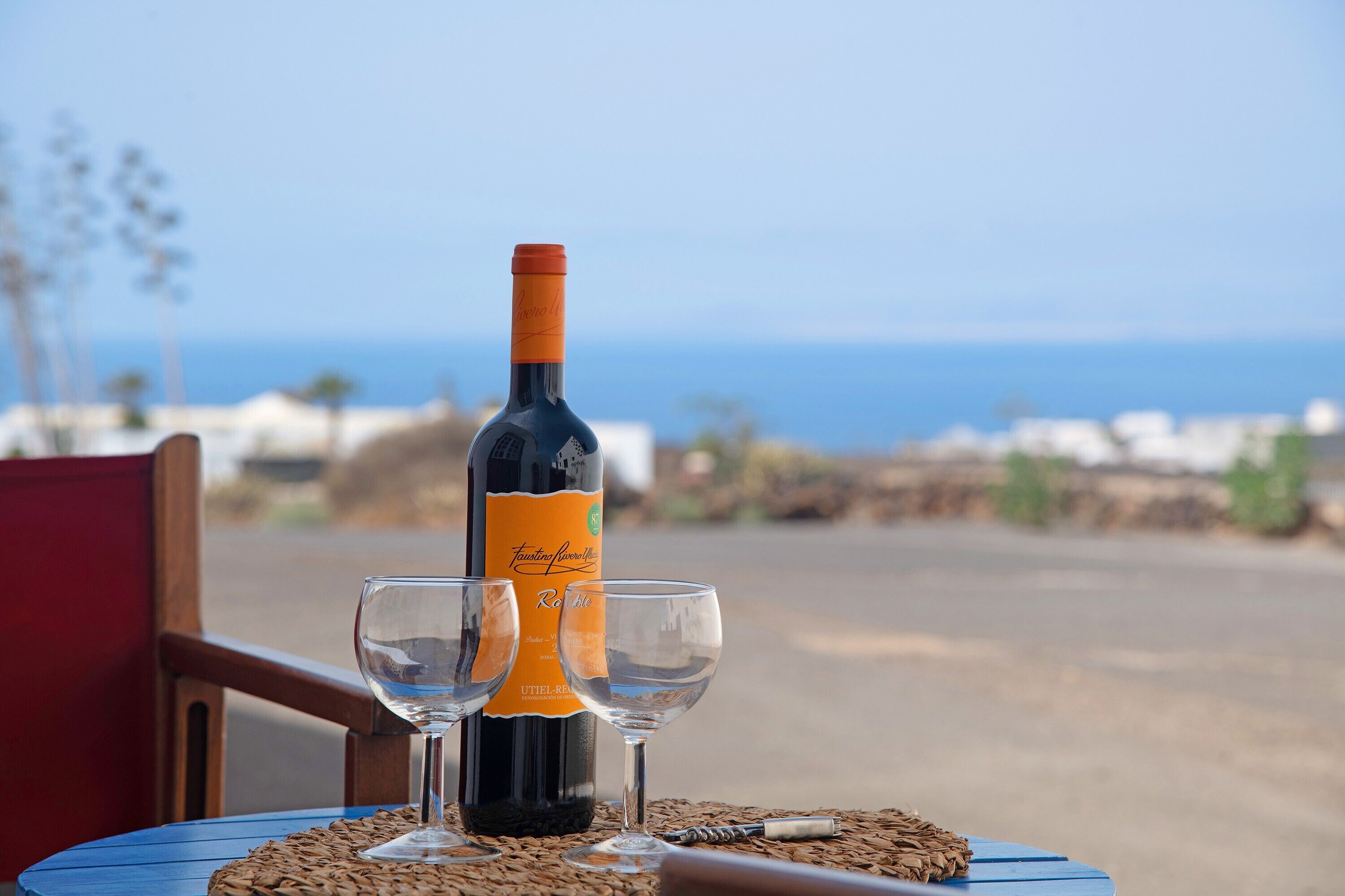 Una botella de vino y dos copas sobre una mesa con vista al océano.