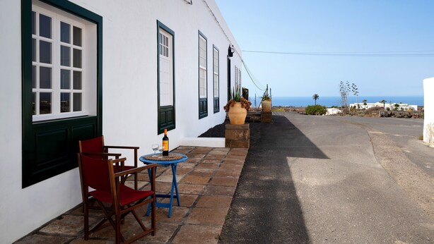 Un bâtiment blanc avec une terrasse dallée, une table et une chaise, et une bouteille de vin.