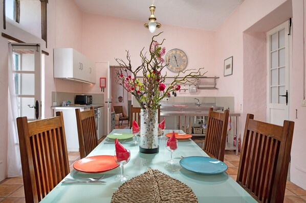 A dining table with chairs, a vase with flowers, and a clock on the wall.