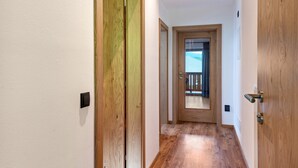 Un couloir avec des portes en bois, un interrupteur et une vue sur un balcon.
