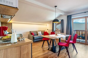 A modern kitchen with a built-in stove, a dining area with a table and chairs, a sofa, and a balcony with a view.