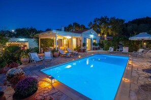 Una piscina con sillones de descanso y un patio techado.